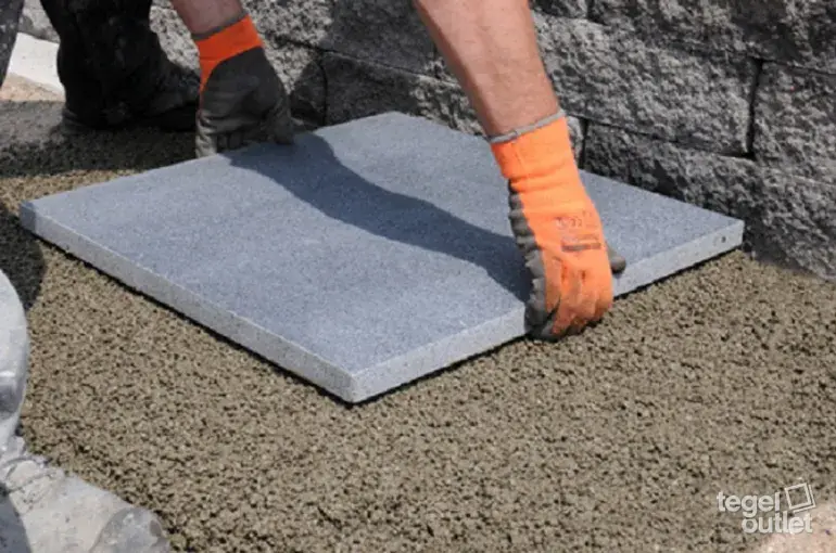 Un carreau d'extérieur gris est posé sur un lit de sable stabilisé