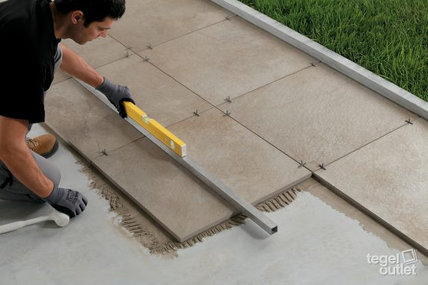 Le carreleur pose des carreaux extérieurs beiges dans la colle et les vérifie avec un niveau